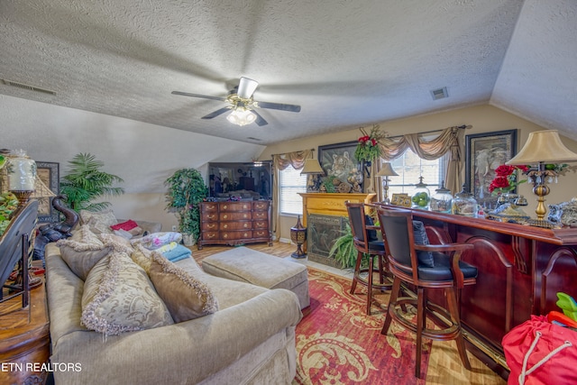 living room with a textured ceiling, ceiling fan, wood-type flooring, and vaulted ceiling