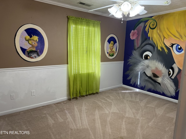 spare room featuring visible vents, a ceiling fan, wainscoting, crown molding, and carpet floors