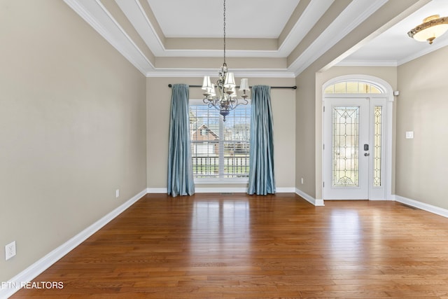 entrance foyer featuring a raised ceiling, a notable chandelier, ornamental molding, and hardwood / wood-style floors