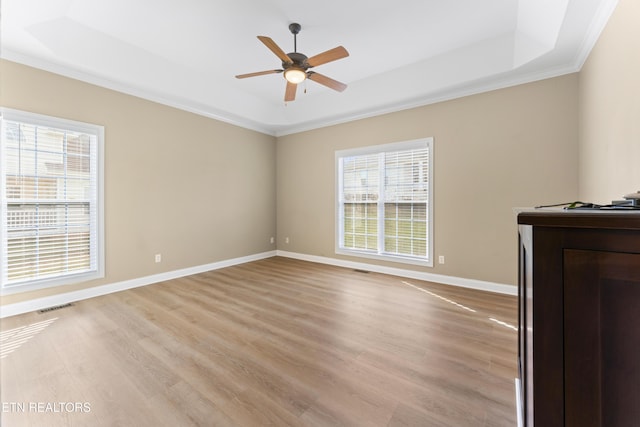 interior space with light hardwood / wood-style floors, a tray ceiling, ornamental molding, and ceiling fan