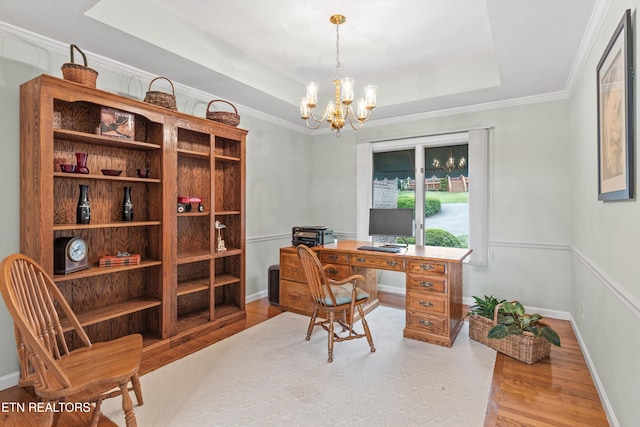 office space featuring ornamental molding, a chandelier, light wood-type flooring, and a tray ceiling