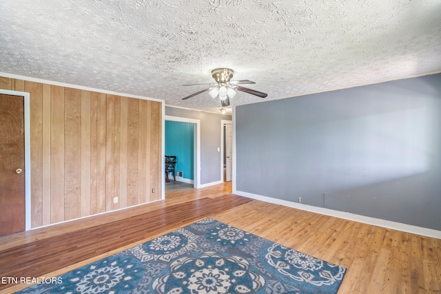 spare room with wood-type flooring, ceiling fan, a textured ceiling, and wood walls