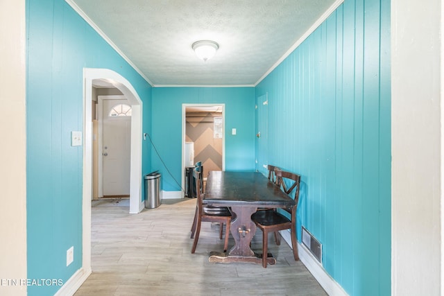 dining space with crown molding, a textured ceiling, and light wood-type flooring