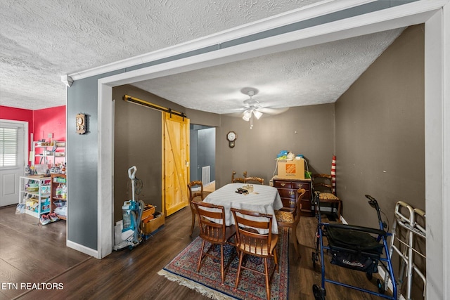 dining space with a textured ceiling, a barn door, dark wood-type flooring, and ceiling fan