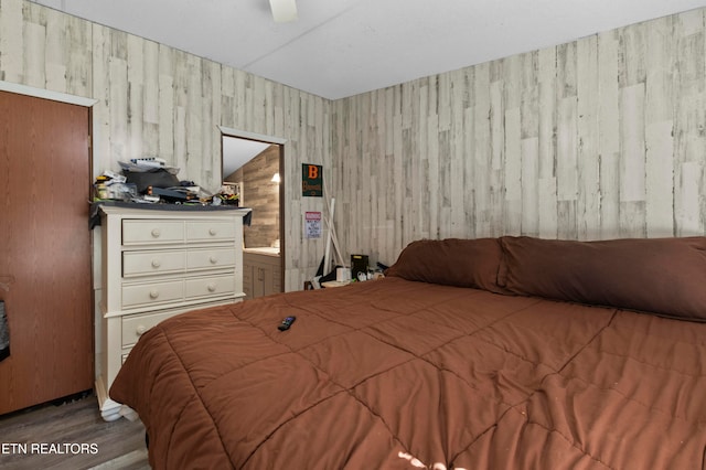 bedroom featuring ensuite bath, ceiling fan, wooden walls, hardwood / wood-style flooring, and lofted ceiling