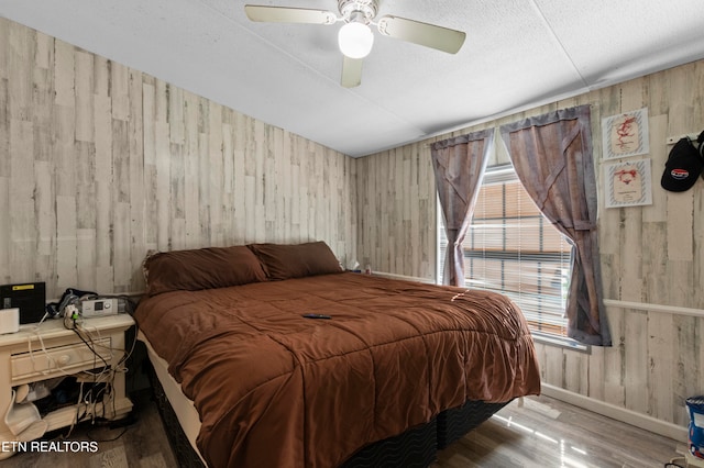 bedroom featuring ceiling fan, wooden walls, and light wood-type flooring