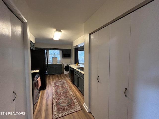 kitchen featuring washer / dryer, sink, black appliances, and hardwood / wood-style flooring