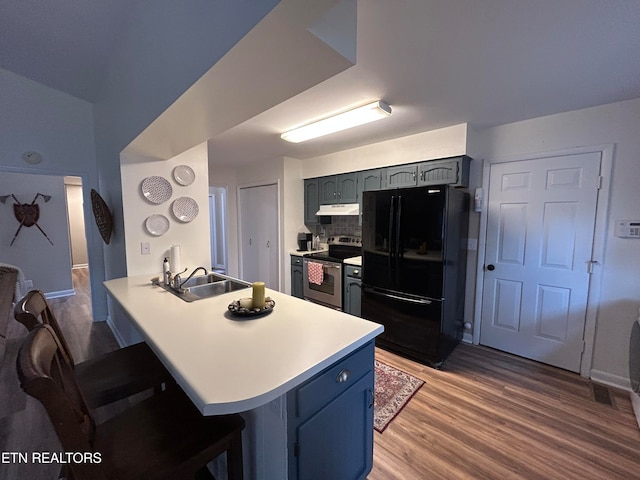 kitchen with a kitchen bar, kitchen peninsula, black fridge, hardwood / wood-style floors, and stainless steel electric range