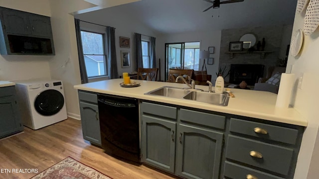 kitchen with washer / clothes dryer, black appliances, sink, light wood-type flooring, and a fireplace