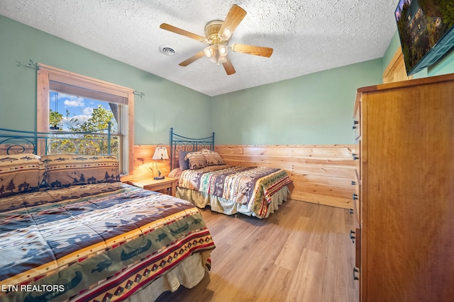 bedroom with wood walls, a textured ceiling, light wood-type flooring, and ceiling fan