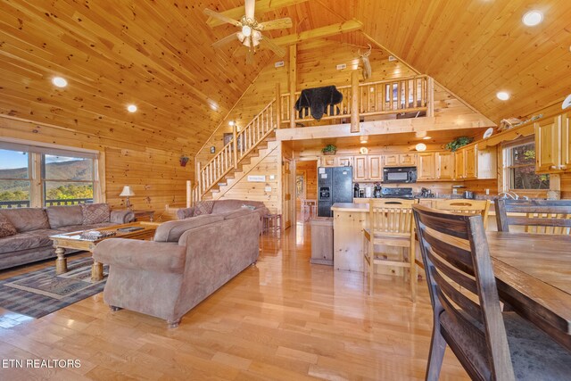 living room with light hardwood / wood-style floors, high vaulted ceiling, and wood walls