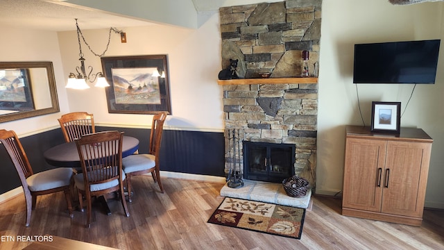 dining area featuring light hardwood / wood-style flooring, a textured ceiling, a notable chandelier, and a fireplace