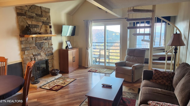 living room with a stone fireplace, vaulted ceiling with beams, and light wood-type flooring