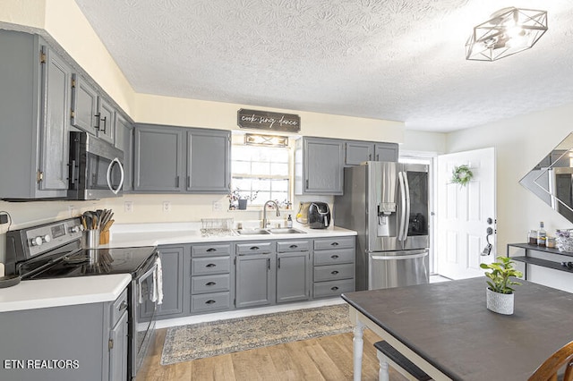 kitchen featuring stainless steel appliances, light hardwood / wood-style floors, a textured ceiling, sink, and gray cabinetry