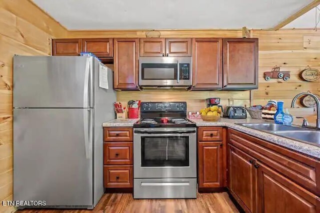 kitchen with wooden walls, light wood-type flooring, sink, and appliances with stainless steel finishes