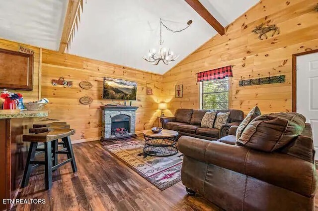 living room with dark hardwood / wood-style flooring, lofted ceiling with beams, wood walls, a chandelier, and a fireplace