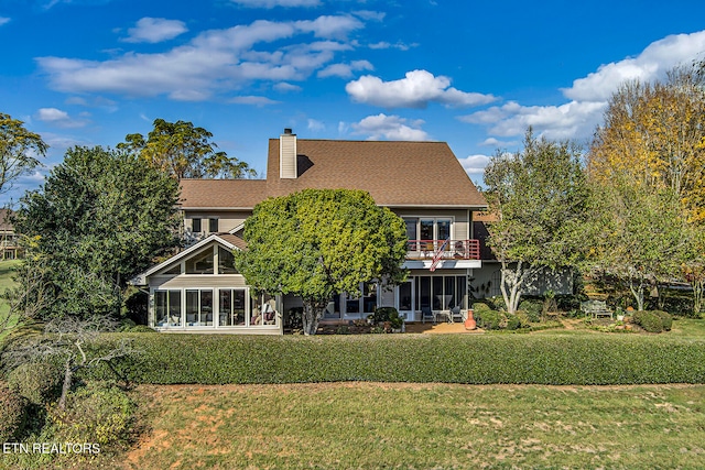 back of house with a chimney, a sunroom, a lawn, and a balcony