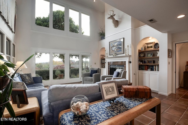 tiled living room featuring built in features, a high ceiling, and a fireplace