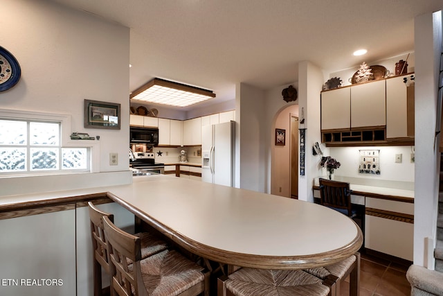 kitchen featuring black microwave, arched walkways, white refrigerator with ice dispenser, electric range, and a kitchen bar