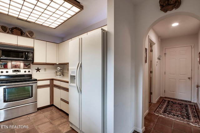 kitchen featuring white refrigerator with ice dispenser, arched walkways, white cabinets, electric stove, and black microwave