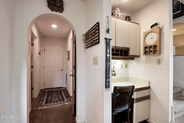 hallway with arched walkways, stairway, baseboards, and tile patterned floors