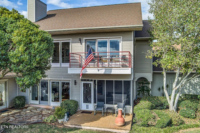 back of property featuring a balcony, a sunroom, a chimney, and roof with shingles