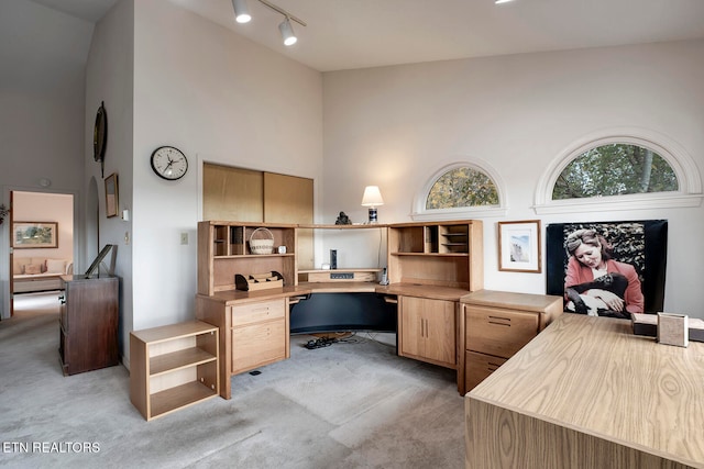 office featuring high vaulted ceiling, built in desk, track lighting, and light colored carpet