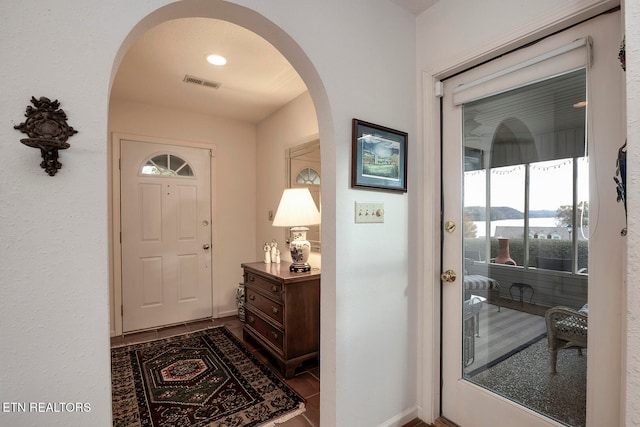 foyer entrance featuring arched walkways, visible vents, and baseboards