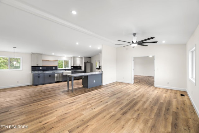 kitchen featuring a kitchen breakfast bar, hanging light fixtures, gray cabinetry, light wood-type flooring, and appliances with stainless steel finishes