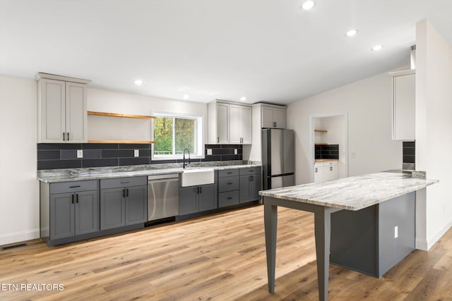 kitchen with gray cabinetry, light hardwood / wood-style floors, stainless steel appliances, vaulted ceiling, and a breakfast bar