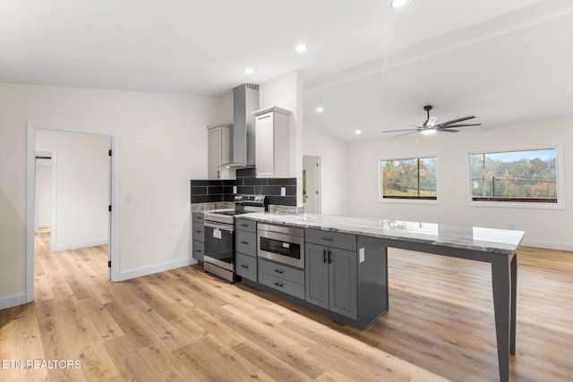 kitchen with gray cabinetry, stainless steel appliances, wall chimney exhaust hood, light stone counters, and light hardwood / wood-style flooring