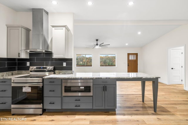 kitchen with appliances with stainless steel finishes, light stone countertops, light hardwood / wood-style flooring, gray cabinets, and wall chimney exhaust hood