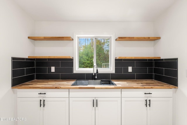 kitchen with white cabinetry, backsplash, wood counters, and sink