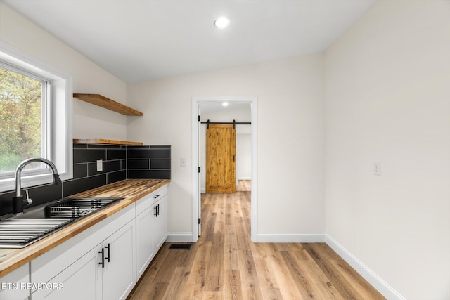 kitchen with sink, a barn door, white cabinetry, light hardwood / wood-style floors, and lofted ceiling