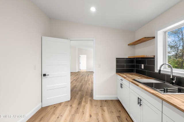 kitchen with lofted ceiling, white cabinetry, light hardwood / wood-style flooring, sink, and butcher block countertops