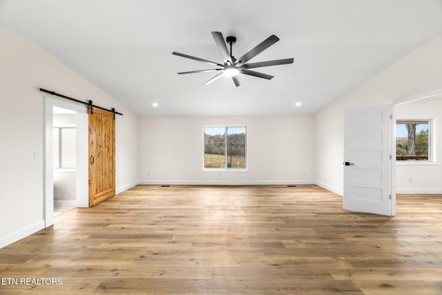 interior space featuring light hardwood / wood-style floors, a barn door, vaulted ceiling, and ceiling fan