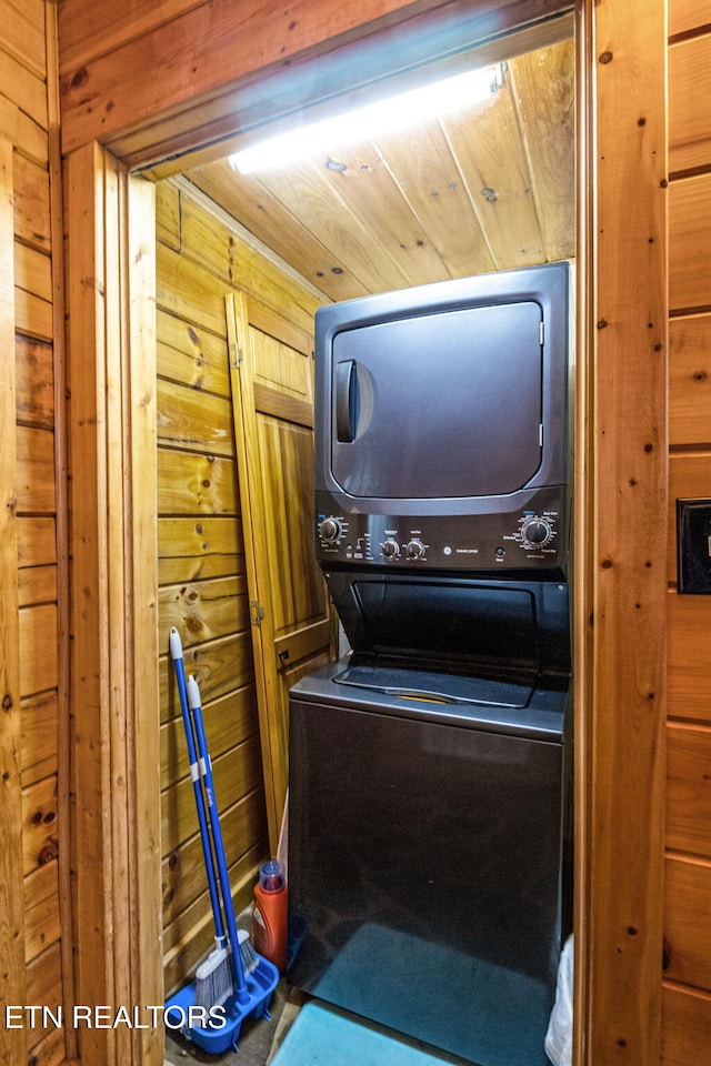 washroom featuring stacked washer and clothes dryer and wooden walls