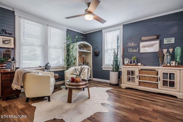 living area with dark wood-type flooring, ceiling fan, a healthy amount of sunlight, and wooden walls