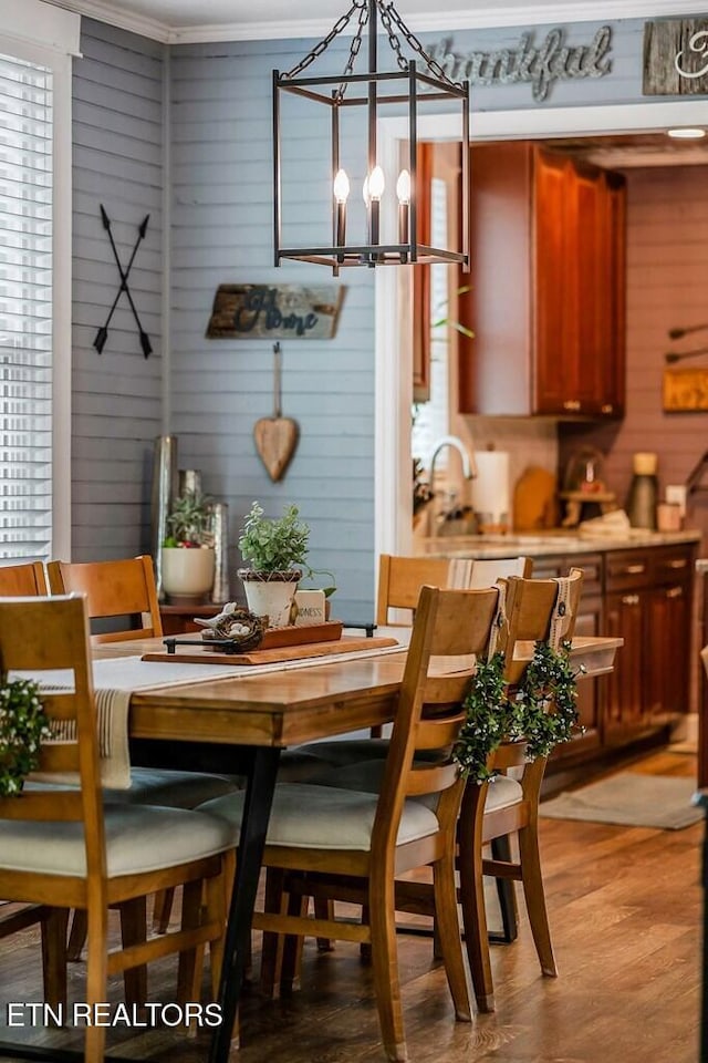 dining space featuring a notable chandelier, ornamental molding, wooden walls, and hardwood / wood-style floors