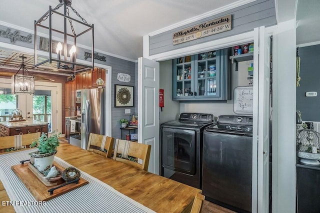 laundry area featuring crown molding, wood walls, a chandelier, and washing machine and clothes dryer