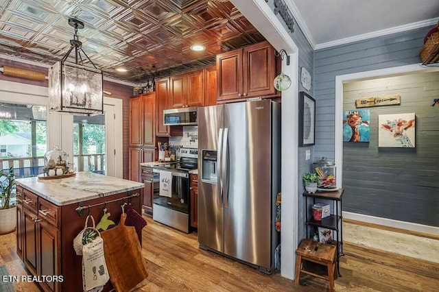 kitchen featuring appliances with stainless steel finishes, ornamental molding, pendant lighting, light hardwood / wood-style floors, and a center island