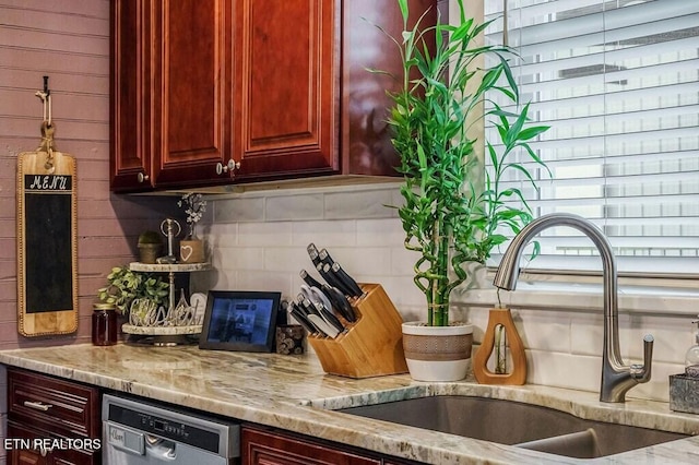 kitchen featuring stainless steel dishwasher, sink, and light stone countertops