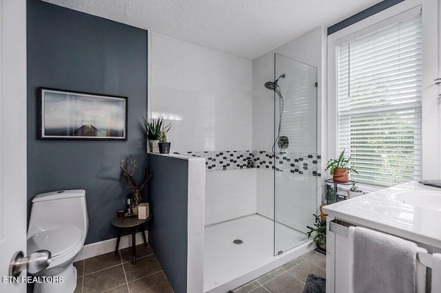 bathroom with vanity, toilet, a tile shower, and tile patterned flooring