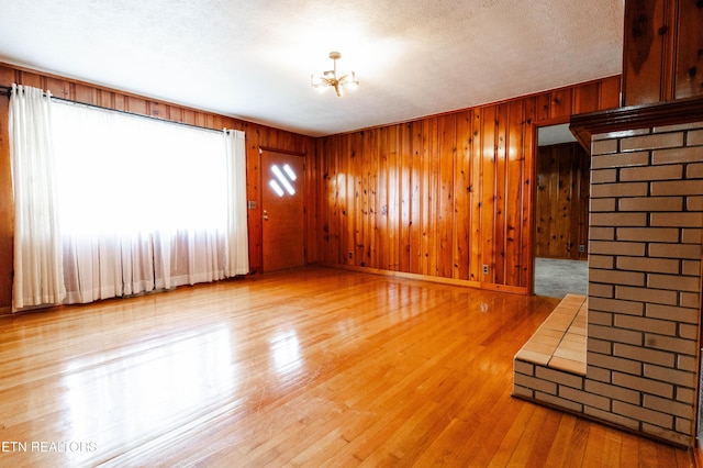 unfurnished room with light wood-type flooring, a textured ceiling, wooden walls, and a notable chandelier