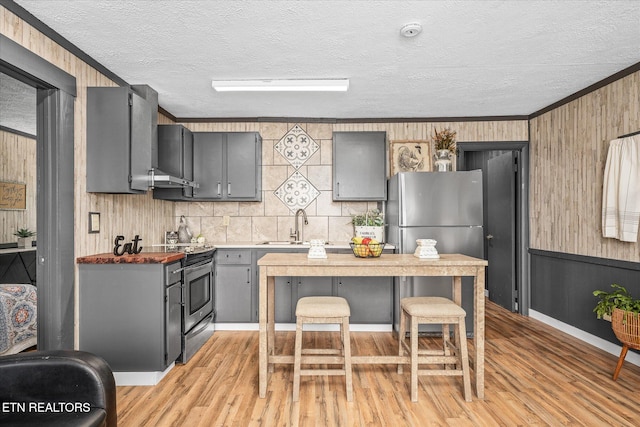 kitchen with light hardwood / wood-style floors, stainless steel appliances, wooden walls, and gray cabinets