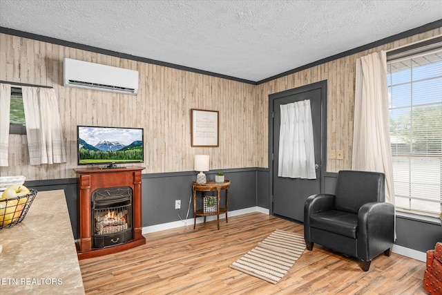 living area with a wall mounted AC, a textured ceiling, light wood-type flooring, ornamental molding, and a fireplace