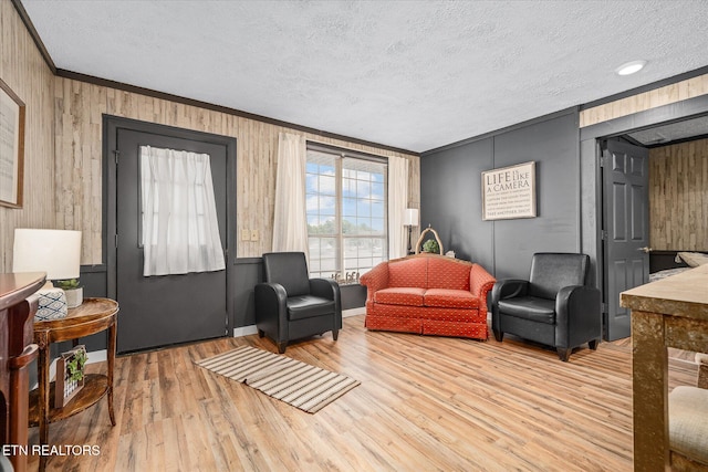 living room featuring crown molding, wood walls, a textured ceiling, and light hardwood / wood-style flooring