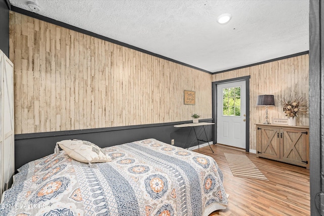 bedroom featuring wooden walls, a textured ceiling, crown molding, and light wood-type flooring