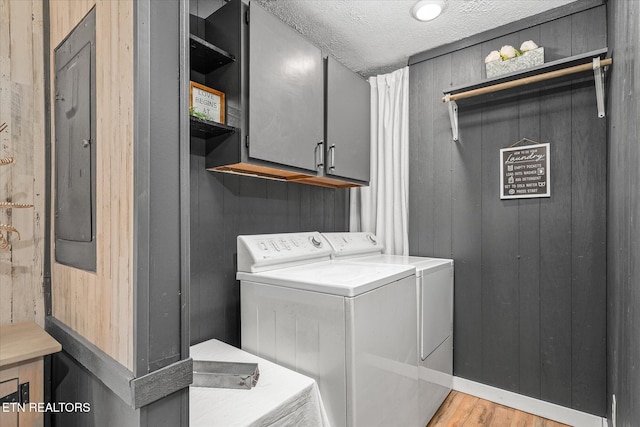 laundry room with cabinets, washer and dryer, a textured ceiling, light hardwood / wood-style flooring, and wood walls