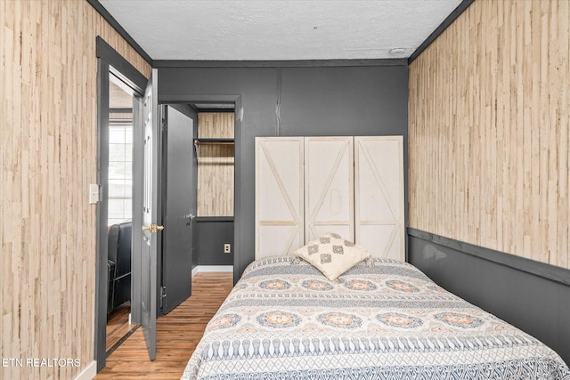 bedroom with wood walls, wood-type flooring, ornamental molding, and a textured ceiling